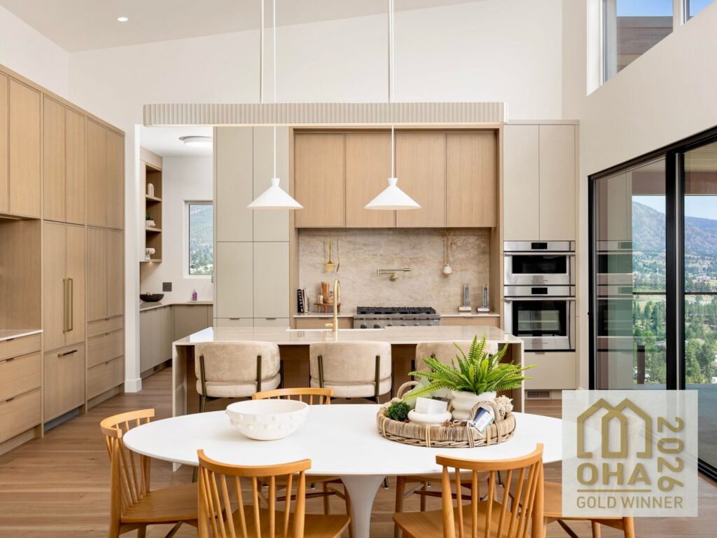 Modern luxury kitchen featuring custom light wood Westwood Cabinetry, a large waterfall island with seating, integrated appliances, and a gold 2026 CHBA Okanagan Housing Awards of Excellence Gold Winner