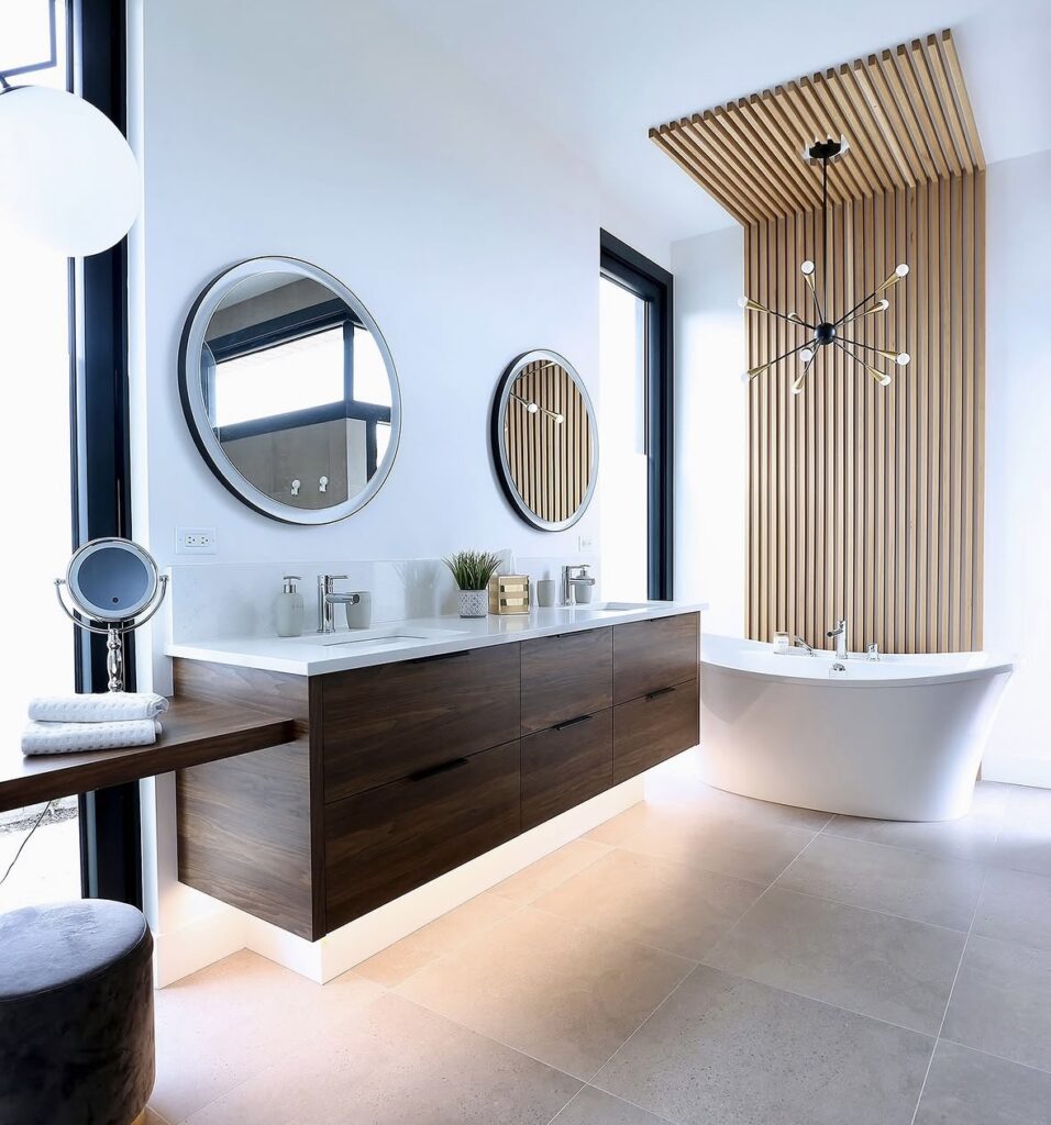 Floating warm wood bathroom vanity with flat-panel cabinetry, white countertop, vessel sink, wall-mounted faucet, round mirror, and modern wall sconces in a neutral bathroom setting. Warm wood bathroom vanities