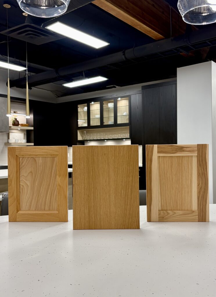 A display of natural wood kitchen cabinet doors including Rift Cut White Oak and Hickory samples showing unique grain patterns and organic textures.