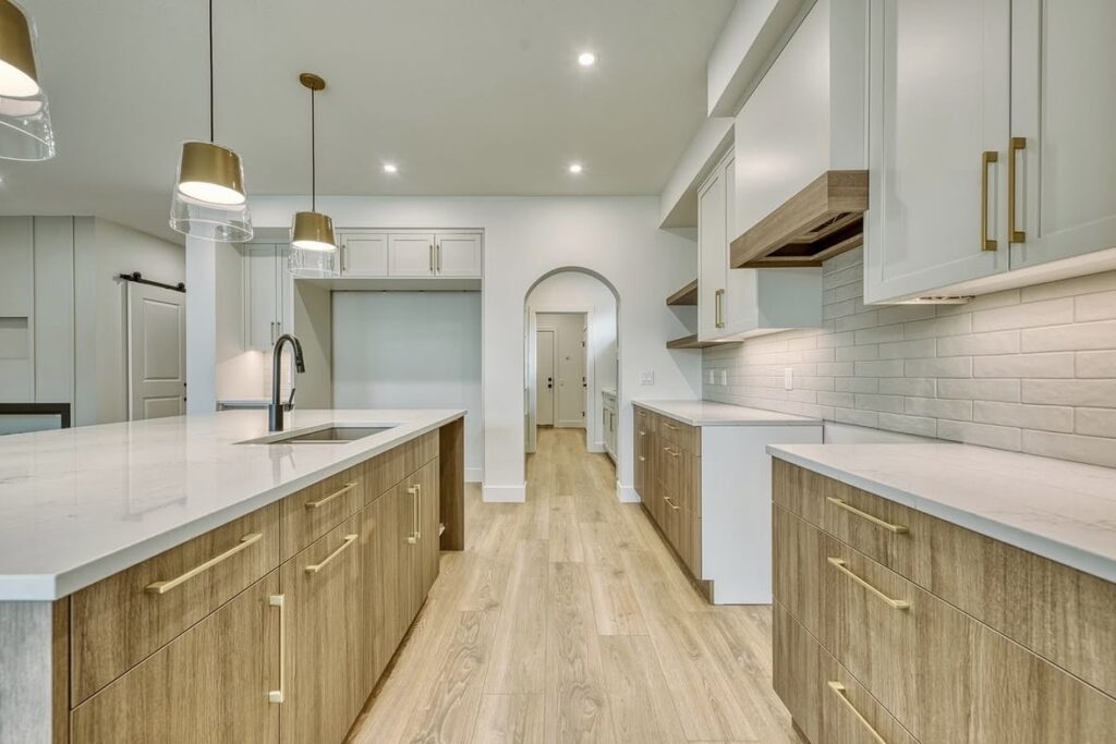 Modern kitchen featuring two-tone kitchen cabinets with light white uppers, warm wood-toned lowers, gold hardware, and an arched doorway transition.