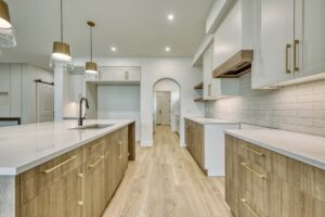Modern kitchen featuring two-tone kitchen cabinets with light white uppers, warm wood-toned lowers, gold hardware, and an arched doorway transition.