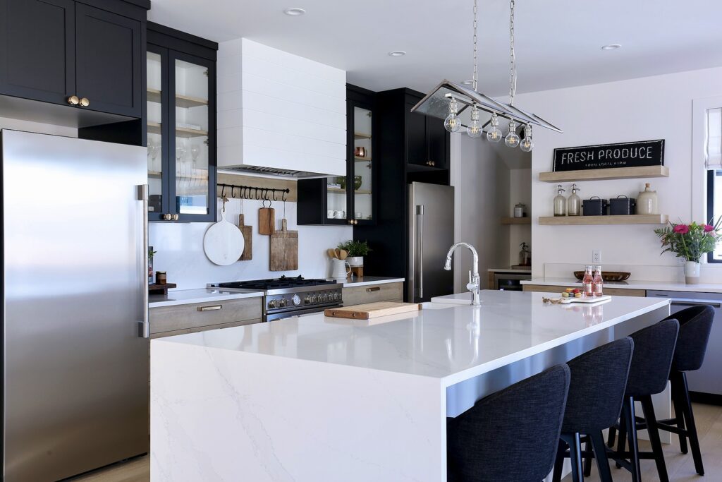 Custom kitchen cabinets in Kelowna featuring a mix of navy uppers, warm wood lower cabinets, and a white marble waterfall island with brass hardware.