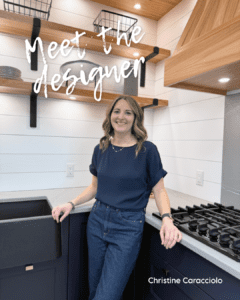 Senior kitchen design expert Christine Caracciolo standing in a modern Westwood Cabinetry kitchen with navy blue lower cabinets and floating wood shelves.