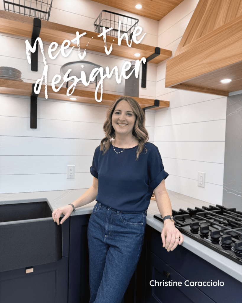 Senior kitchen design expert Christine Caracciolo standing in a modern Westwood Cabinetry kitchen with navy blue lower cabinets and floating wood shelves.