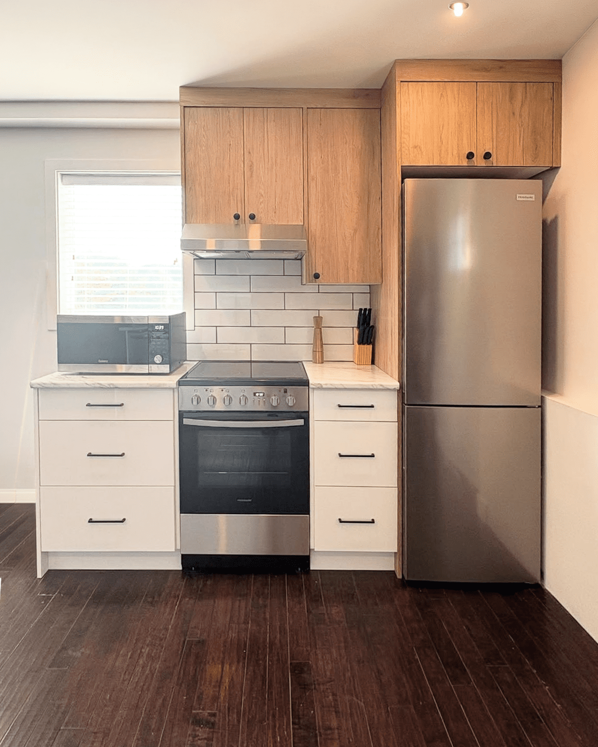 Compact kitchen layout with a stainless steel range and slim refrigerator, featuring white and light oak cabinetry from the Westwood Elements line.