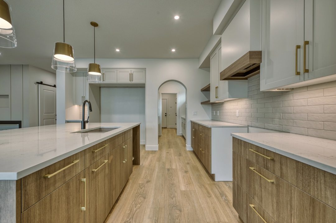 An open concept kitchen designed by a kitchen design expert featuring light oak island cabinetry, gold hardware, white quartz countertops, and a subway tile backsplash.