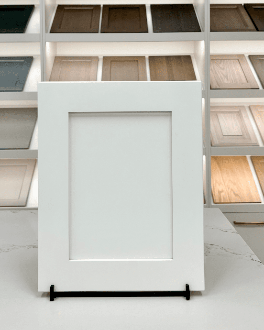 A clean, white Traditional Shaker cabinet door featuring a recessed center panel and wide stiles and rails, displayed on a countertop in a kitchen showroom.