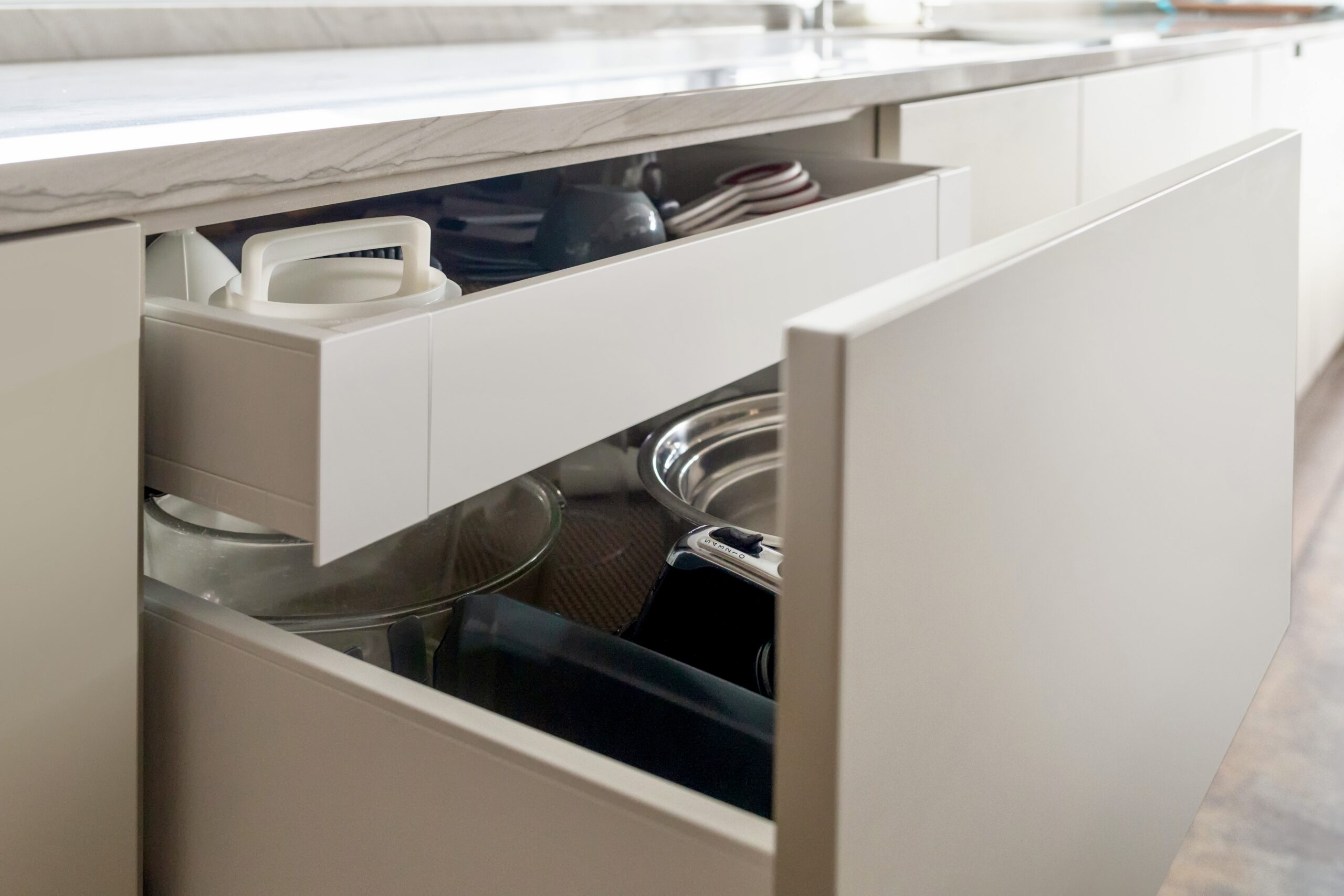 A deep lower cabinet drawer pulled open under a quartz countertop to reveal organized mixing bowls, pots, pans, and small appliances to upgrade your kitchen storage.