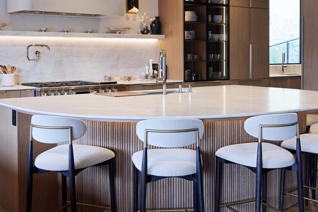 A close-up of an architectural kitchen island highlighting the intricate vertical fluted wood panels on a radiused base, topped with a thick white stone countertop and gold accents.
