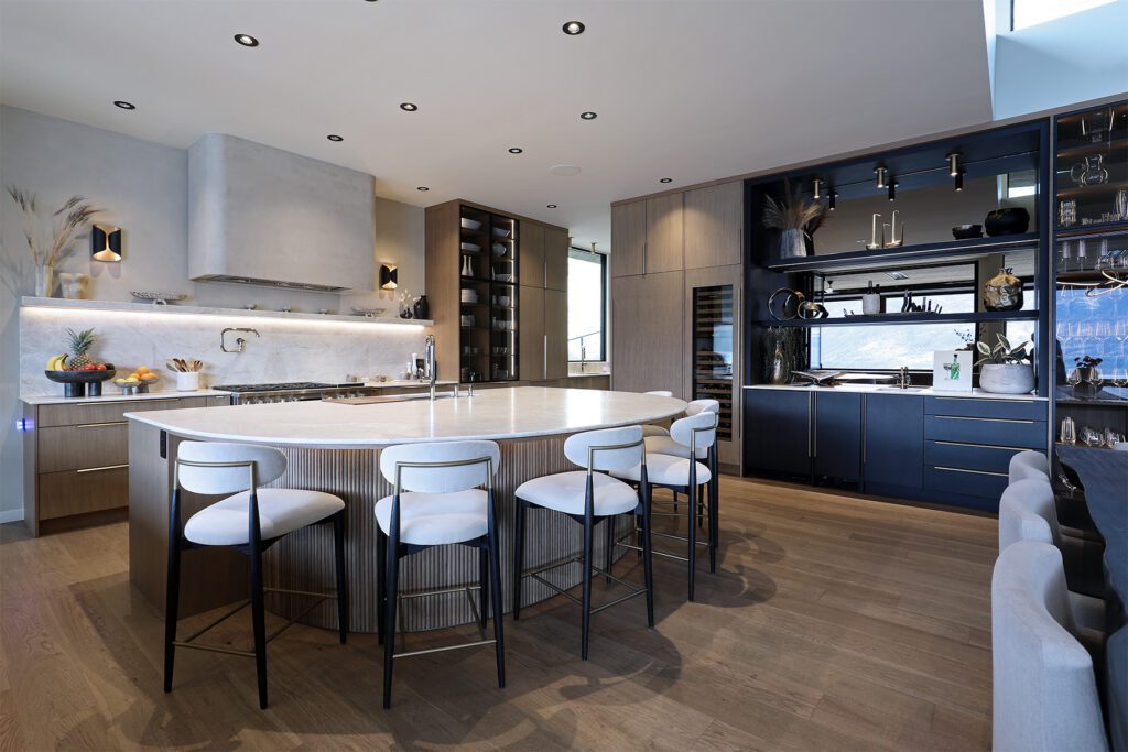 A luxury modern kitchen featuring a large architectural kitchen island with a curved wood base and fluted detailing, paired with white modern barstools and sleek oak cabinetry.