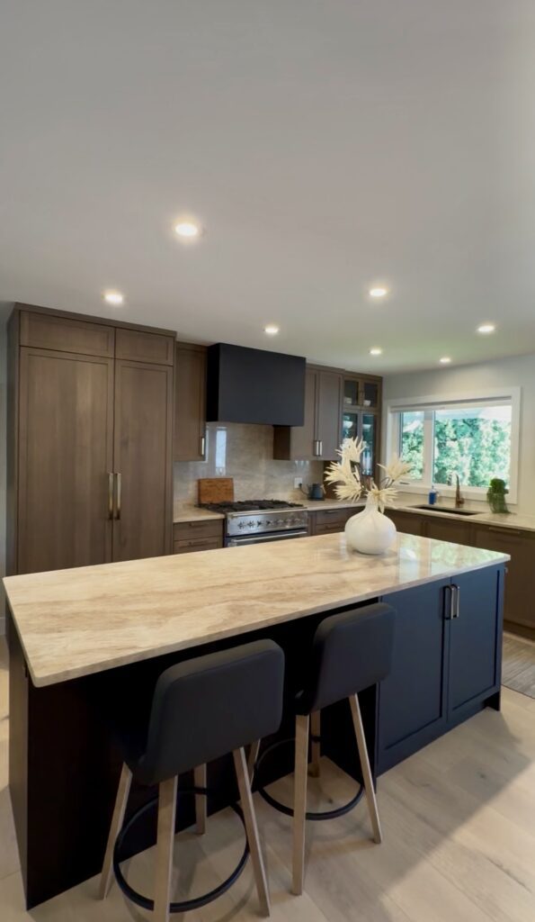 Custom kitchen cabinetry featuring warm wood tones, a large island with stone countertops, black bar stools, and a black range hood.