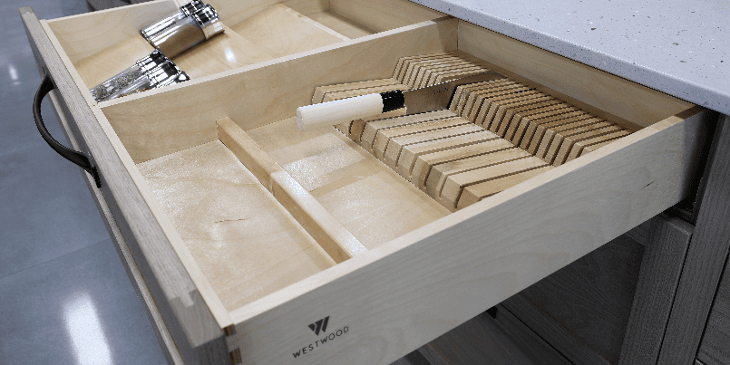 An open custom wood kitchen drawer featuring built-in custom drawer inserts, including a knife block slot holding a kitchen knife and organized compartments holding spice jars.